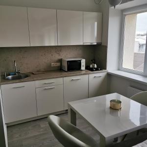 a kitchen with white cabinets and a table and a microwave at Apartamentai prie bažnyčios in Palanga