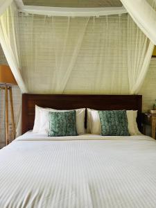 a bed with white sheets and green pillows at Depong House in Ubud