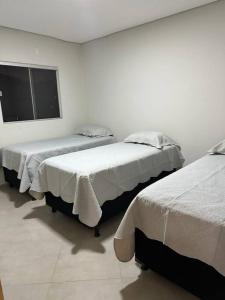 Dieses weiße Zimmer verfügt über 2 Betten und ein Fenster. in der Unterkunft Apartamento com vista para palco festival in Chapada dos Guimarães