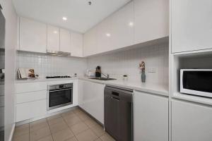 a white kitchen with white cabinets and a microwave at Entire home with parking in Parramatta in Sydney