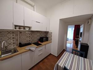 cocina con armarios blancos, fregadero y mesa en Hero's Square Apartment en Budapest