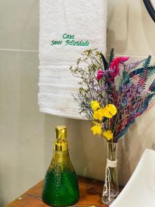 a green bottle and a vase of flowers on a table at Casa Santa Felicidade - Gravatá in Gravatá