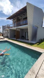une personne se posant dans une piscine en face d'une maison dans l'établissement Flor de Cacto Beach Home, à São Miguel do Gostoso