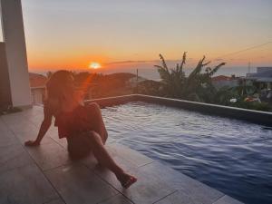 a woman sitting next to a swimming pool with the sunset at Cocon detente a Case pilote, chambre chez l'habitant in Case-Pilote