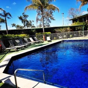 a large swimming pool with lounge chairs next to a house at John Hunter Motel Muswellbrook in Muswellbrook