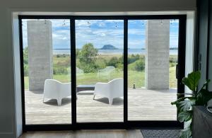 dos sillas blancas sentadas frente a una puerta corredera de cristal en Guesthouse @ Te Puna, en Tauranga