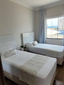 2 camas en una habitación blanca con ventana en Sobrado com garagem e churrasqueira, en Tijucas