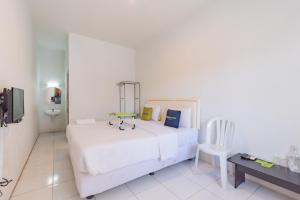 a white bedroom with a bed and a chair at Urbanview Hotel Kazanan Lembang Bandung by RedDoorz in Bandung