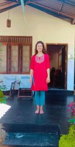 kobieta w czerwonej sukience stojąca przed domem w obiekcie Jayanika Residence w Tangalli