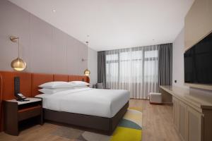 Home2 Suites by Hilton Guangzhou Baiyun Airport West في هوادو: غرفة فندقية بسرير وتلفزيون بشاشة مسطحة