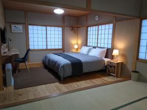 a bedroom with a bed and a desk and windows at Robin's Lodge in Iiyama