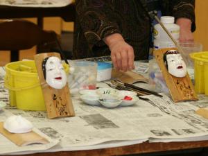Uma mulher está a fazer máscaras numa mesa. em Fureaihouse Shiodu no Sato em Sado