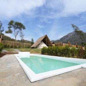 a swimming pool in front of a house with a thatch roof at RoomQuest Kid Tung Khao in Ban Huai Sok Noi