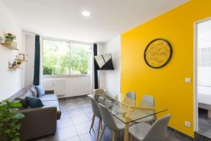 een woonkamer met een glazen tafel en een gele muur bij Sereniva - Appartement Familial 2 chambres in Reims