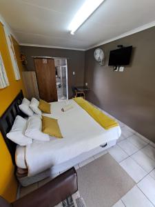 uma cama grande com lençóis brancos e almofadas amarelas em Aviators Retreat B&B em Krugersdorp