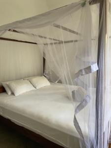 a bed with a canopy with white sheets and pillows at Casa Tharin Madiha in Matara