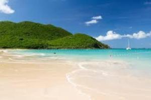 einen weißen Strand mit einer grünen Insel im Hintergrund in der Unterkunft Joli appartement indépendant au calme. in Marigot