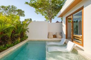a pool with two white chairs next to a house at Las Hermanas Villa by MAR Bali in Dalung