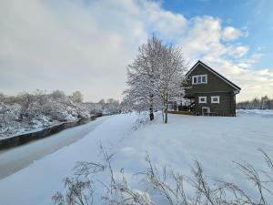 una casa está cubierta de nieve junto a un río en Jõesuu saunamaja, en Valga