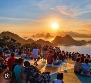 grupa ludzi siedzących na ziemi obserwujących zachód słońca w obiekcie Cantinho da Paz w mieście Niterói