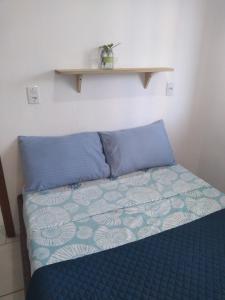 a bed with blue pillows and a shelf on the wall at Casas do Manoel in Praia do Rosa