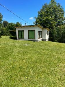 une petite maison blanche sur un champ herbeux dans l'établissement Casa de campo, à Lago Ranco