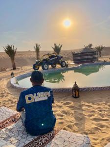 a man sitting next to a pool in the desert at Dubaicanam Camp in Dubai
