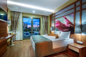 Alan Xafira Deluxe Resort & Spa-ULTRA ALL INCLUSIVE في ألانيا: غرفة فندقية بسرير ونافذة كبيرة