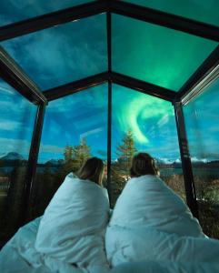 dos personas tumbadas en la cama mirando la aurora boreal en WonderInn Arctic, en Utstrand