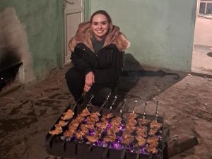 a woman is sitting next to a grill with pastries at Xinaliq İzzet's Riverside Home Stay in Xınalıq