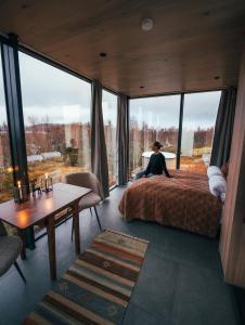 una mujer sentada en una cama en una habitación con ventanas grandes en WonderInn Arctic en Utstrand