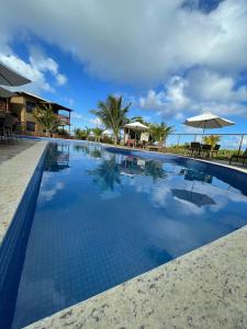 a large swimming pool with tables and umbrellas at CASA Beira Mar Pé na Areia - Itacimirim Bahia in Camaçari