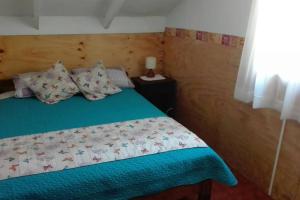 a bedroom with a bed with a green blanket and pillows at Cabaña a metros de la playa San Ignacio, Niebla in Valdivia