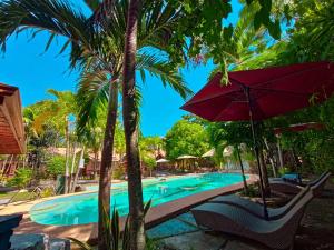 a resort pool with a red umbrella and palm trees at Coco Grove Nature Resort in Himensulan