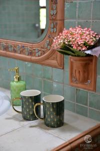 two coffee cups sitting on a bathroom counter with a vase of flowers at Pávakakas Vendégház in Vác