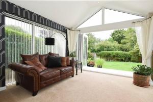 a living room with a leather couch in front of a window at Beautiful Meon Valley Family Home in Shedfield