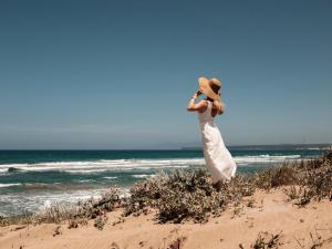 uma mulher de vestido branco parada na praia em Is Arenas Resort em Narbolia