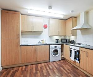 a kitchen with wooden cabinets and a washing machine at Bright & Immense 2 BDR Flat near Excel Center in London