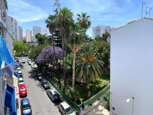 una calle de la ciudad con coches aparcados y palmeras en Los Guindos, en Málaga