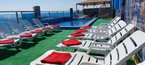 a row of white chairs with red cushions next to a swimming pool at Blue Waves Abu Halifa أمواج الخليج الزرقاء in Kuwait