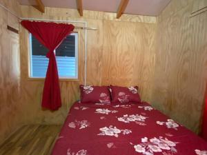 a bedroom with a red bed with a window at Cabañas Don Esteban in Tortel