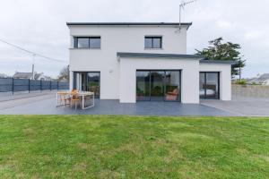 ein weißes Haus mit einer Terrasse und Gras in der Unterkunft KER STIVELL - Superbe maison neuve à 2 pas de la mer in Landunvez