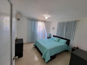 a bedroom with a bed with a blue comforter and two windows at Acogedor apartamento a un paso de la playa in Juan Dolio