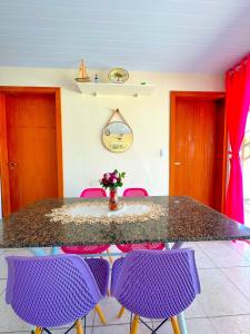 einen Tisch mit lila Stühlen und eine Vase mit Blumen in der Unterkunft Casa de Anita Pinheira 30m da praia in Palhoça