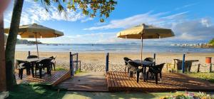 una terraza de madera con mesas y sombrillas en la playa en Pousada Enseada São Miguel de frente para o mar, en Penha