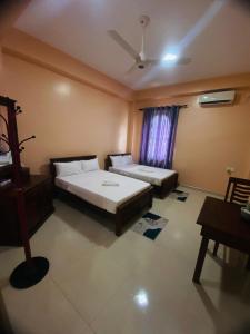 a bedroom with two beds and a table and a window at Ajith Putha Grand in Madampe
