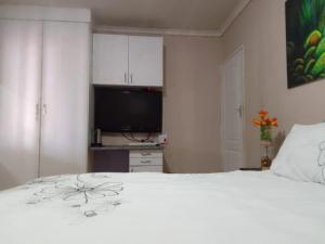 a bedroom with a white bed and a flat screen tv at Garden View Guesthouse Klinker in Johannesburg