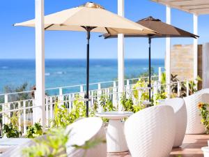 a patio with white chairs and umbrellas and the ocean at Umi No Terrace Yomitan Toya in Yomitan