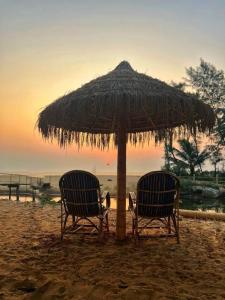 two chairs under a straw umbrella on the beach at The Goko Social in Gokarna