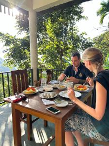 un homme et une femme assis à une table mangeant de la nourriture dans l'établissement Nature Green Hotels On Rock Home Ella, à Ella